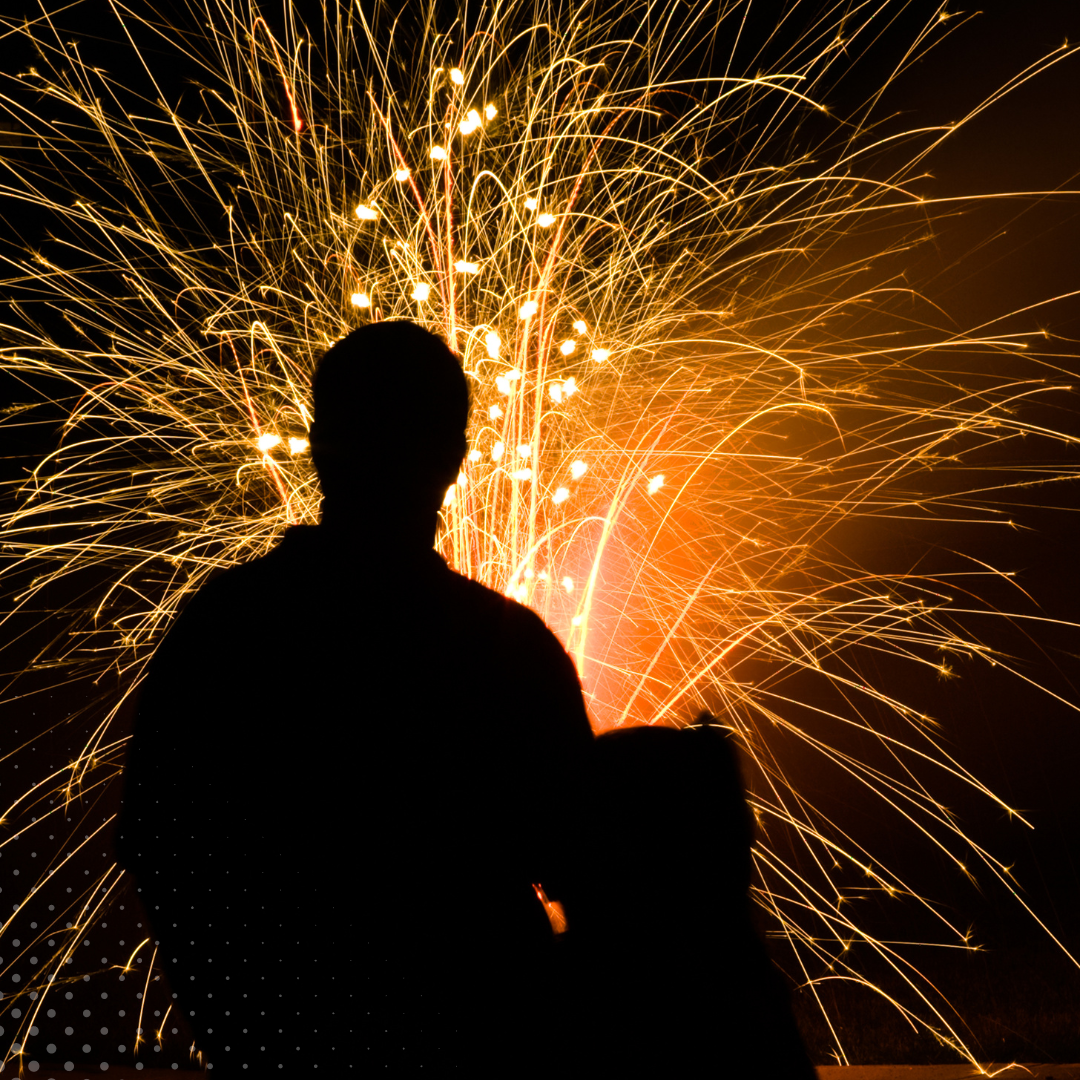 Vivid fireworks light up the sky behind a person's silhouette