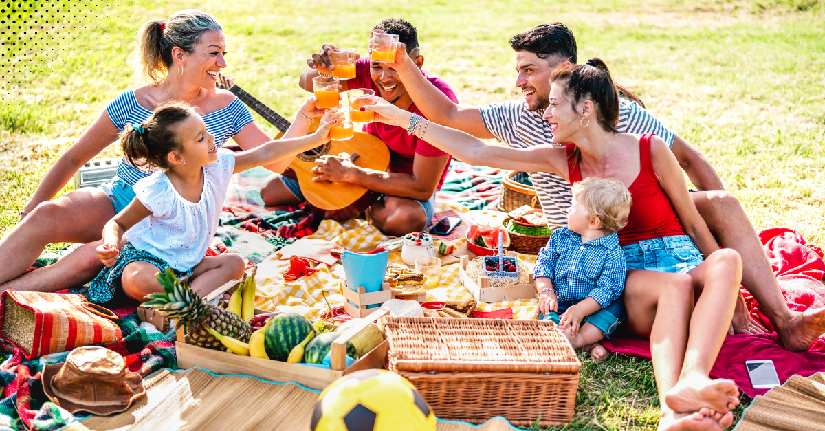 Two families enjoying a lively outdoor picnic with food and drinks, creating joyful fall memories together. 