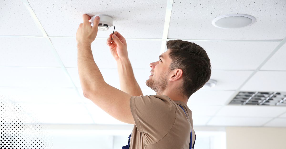 young man installing or checking a smoke detector on a ceiling