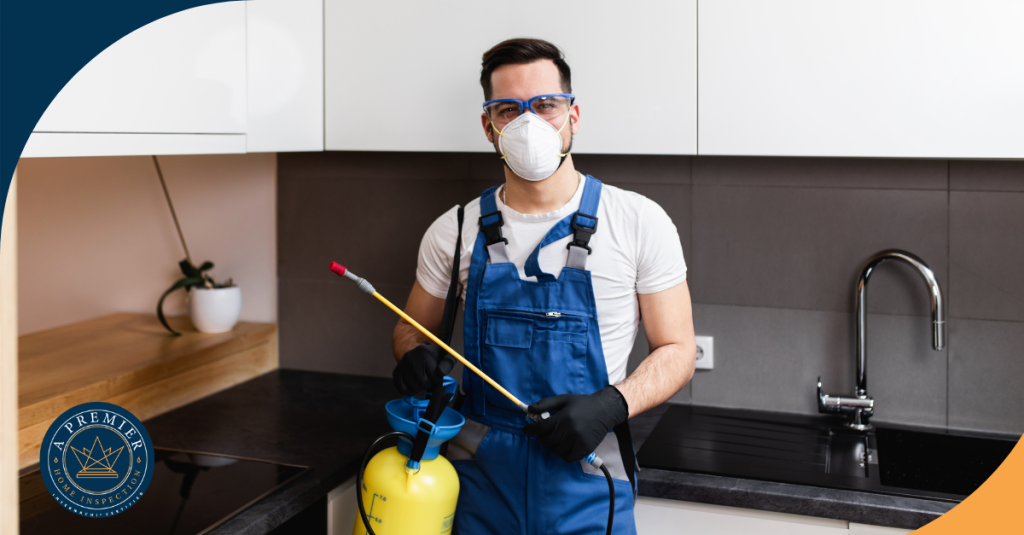 Professional pest control technician in blue overalls and protective gear holding a sprayer in a modern kitchen.