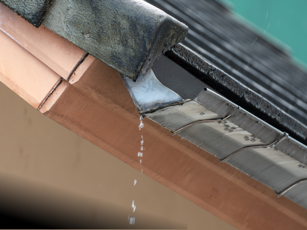 Water spilling out of a roof's gutter in a downpour.