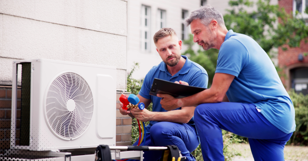 Two HVAC technicians checking outdoor air conditioning unit with gauges