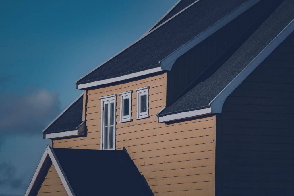 An exterior view of a yellow home's roofline against a blue sky, showcasing the shape and various parts of a roof frame.