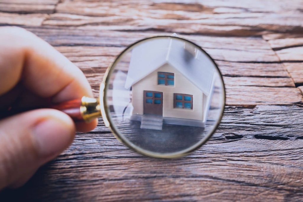 Magnifying glass examining a miniature house, illustrating how A Premier Home Inspection helps buyers thoroughly evaluate a property.