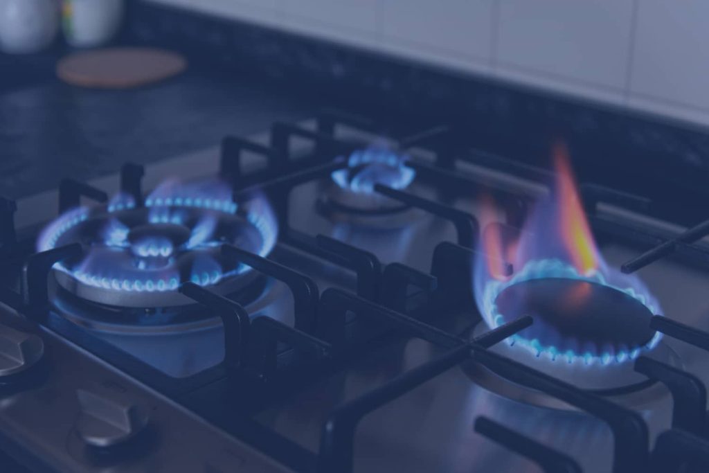 A close-up shot of a gas cooktop with multiple burners lit with blue flames in a dimly lit setting.
